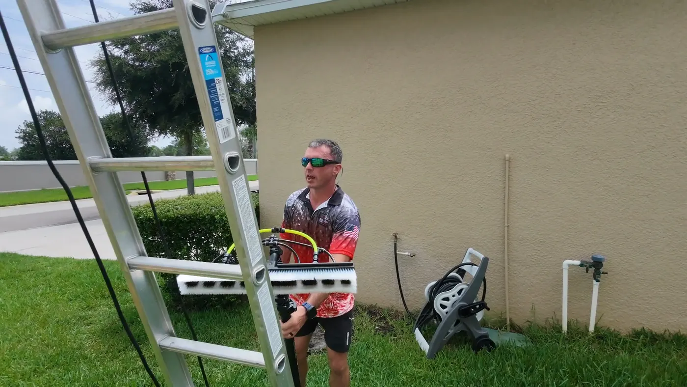 Iron Shield technician at an extension ladder with a long-reach application brush against a stucco exterior wall