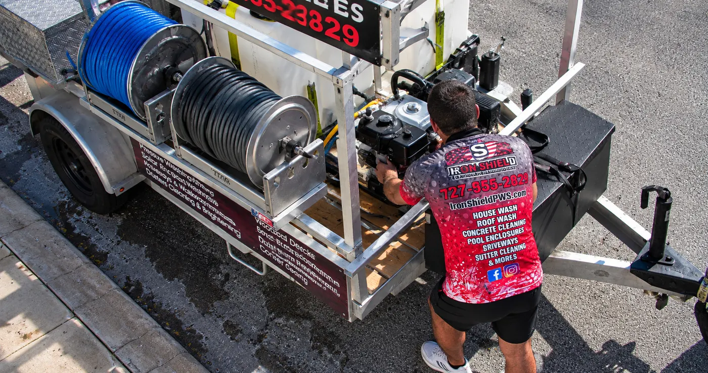 Iron Shield technician making a final check of the pressure washer unit, hoses and engine on the service trailer