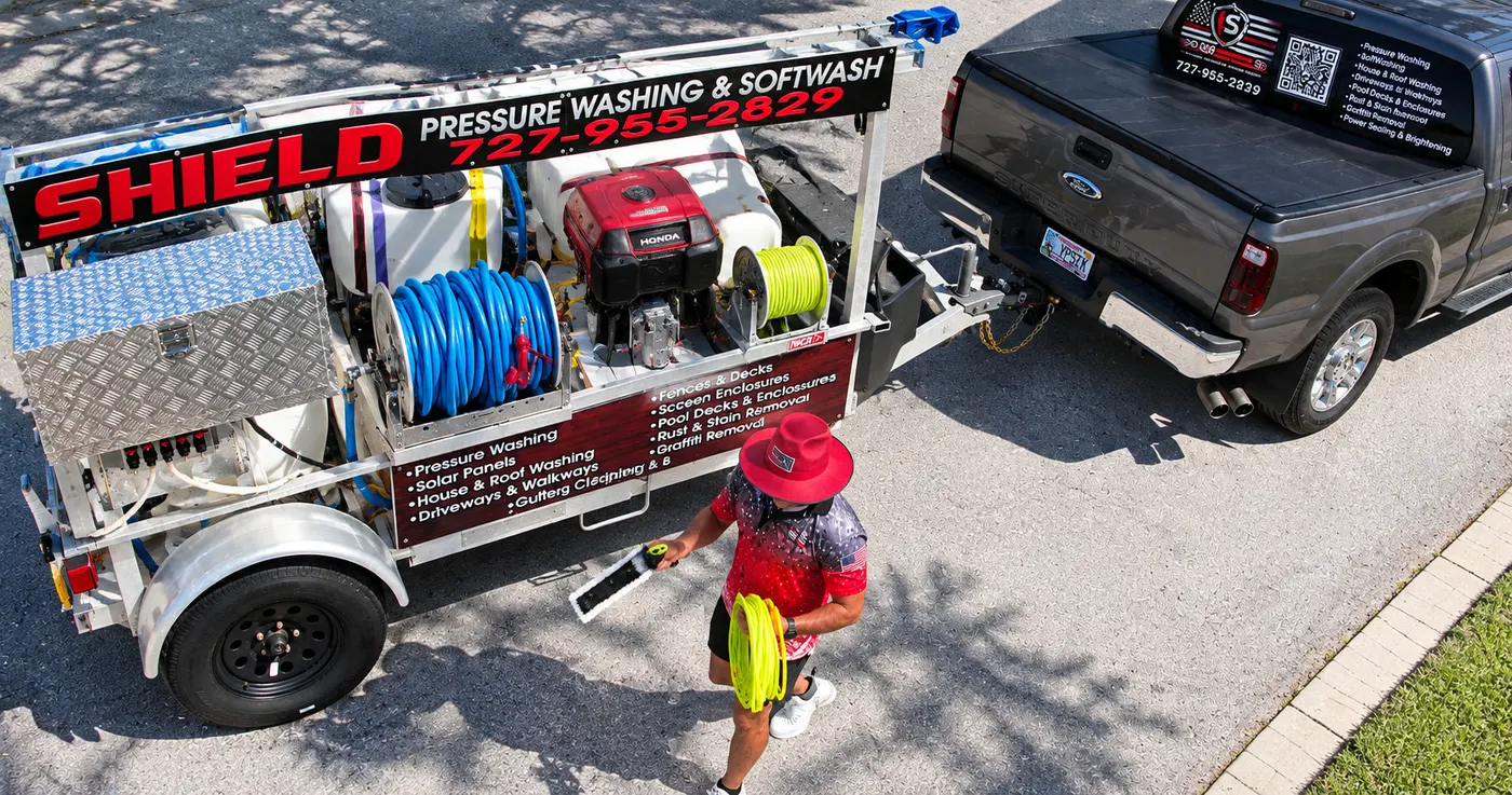 Iron Shield technician taking a cleaning brush and hose from the branded pressure washing trailer
