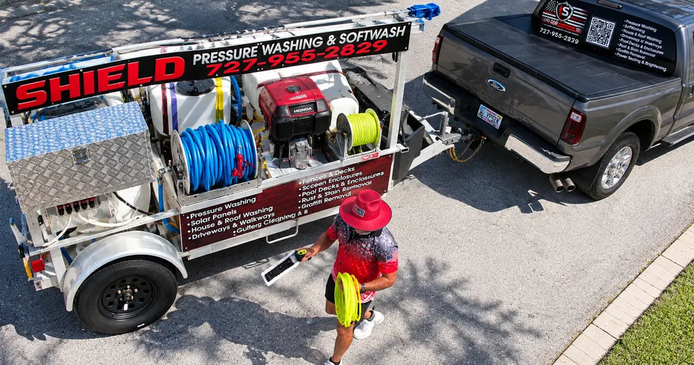 Iron Shield technician taking a cleaning brush and hose from the branded pressure washing trailer