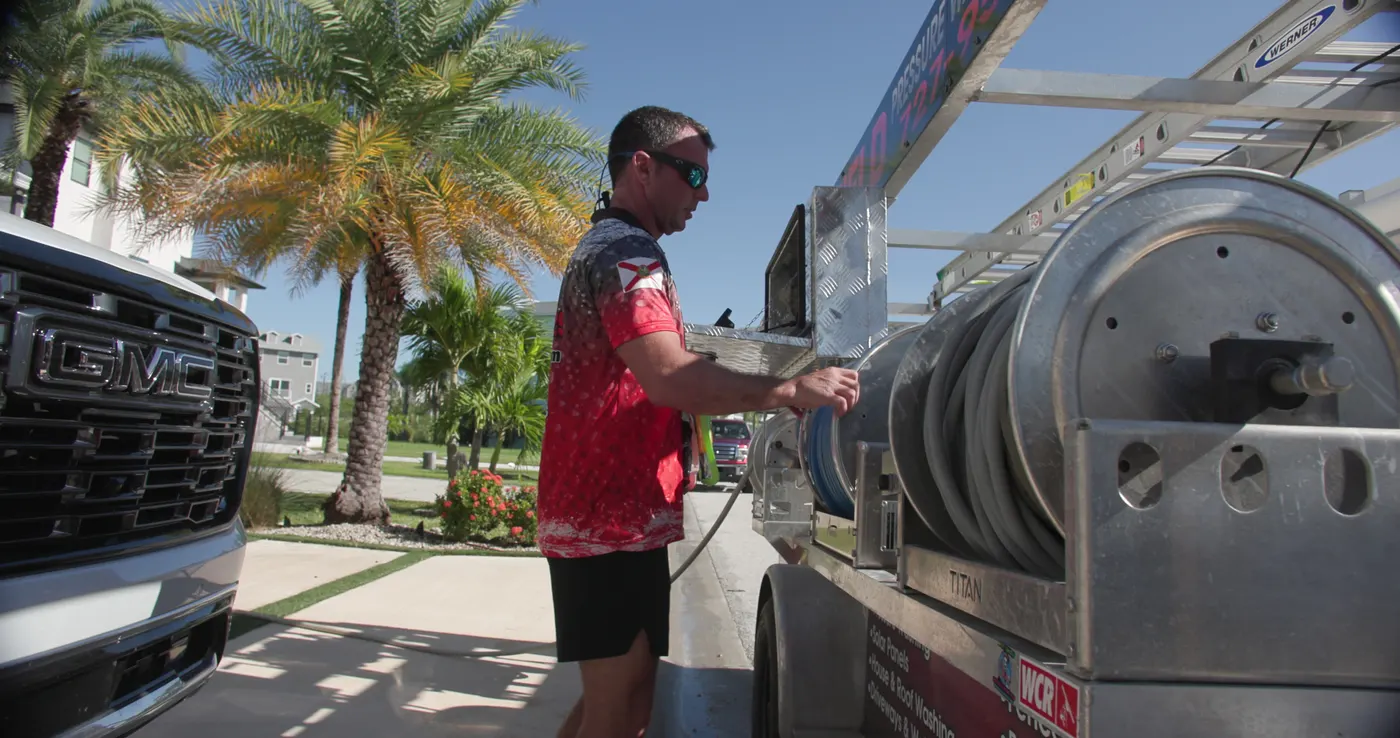 Iron Shield technician pulling hose from the reel on the service trailer before a dumpster pad cleaning