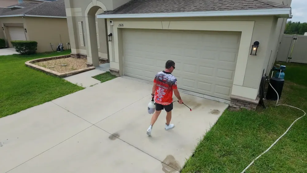 Iron Shield technician spraying cleaning solution onto stained concrete directly in front of a garage door