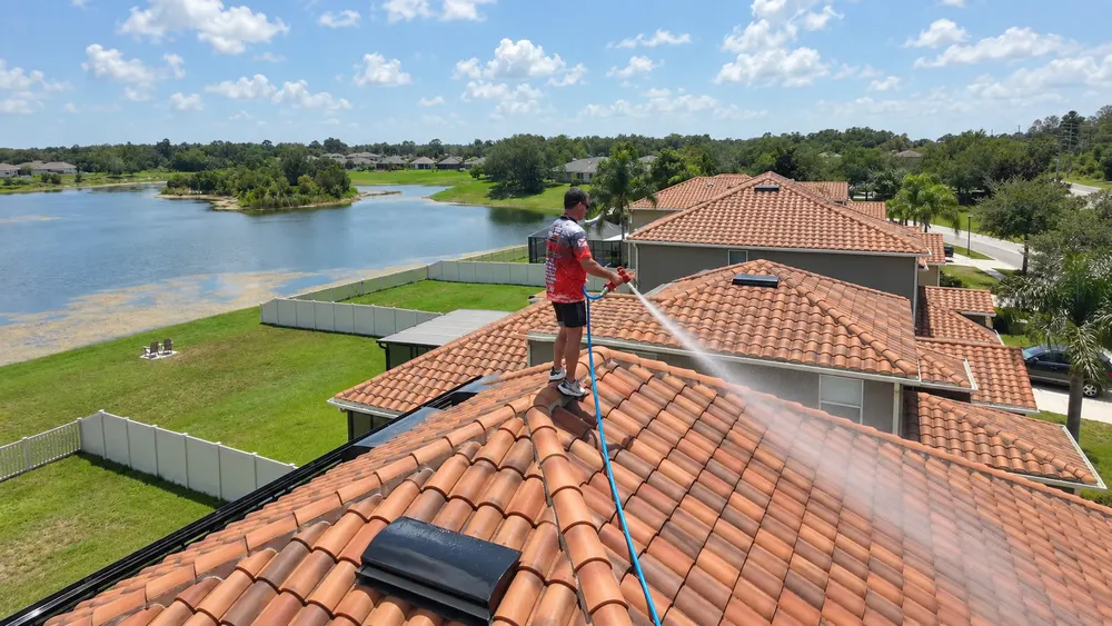 Iron Shield technician spraying a controlled wash across a terracotta barrel tile roof beside a lake