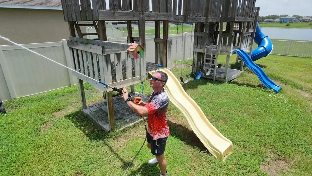 Iron Shield technician spraying the deck and rails of a wooden play structure with a yellow slide
