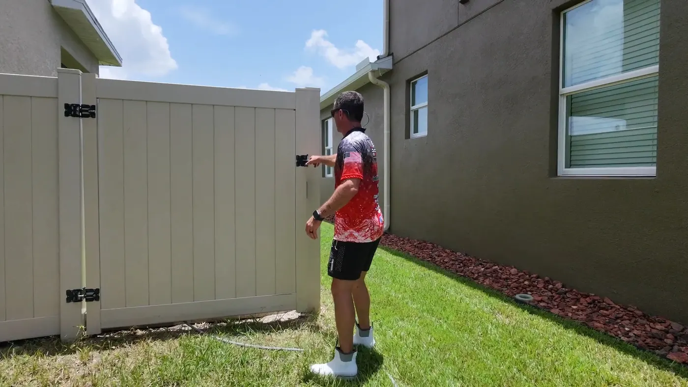 Iron Shield technician working along a white vinyl fence where it meets the side wall of the house