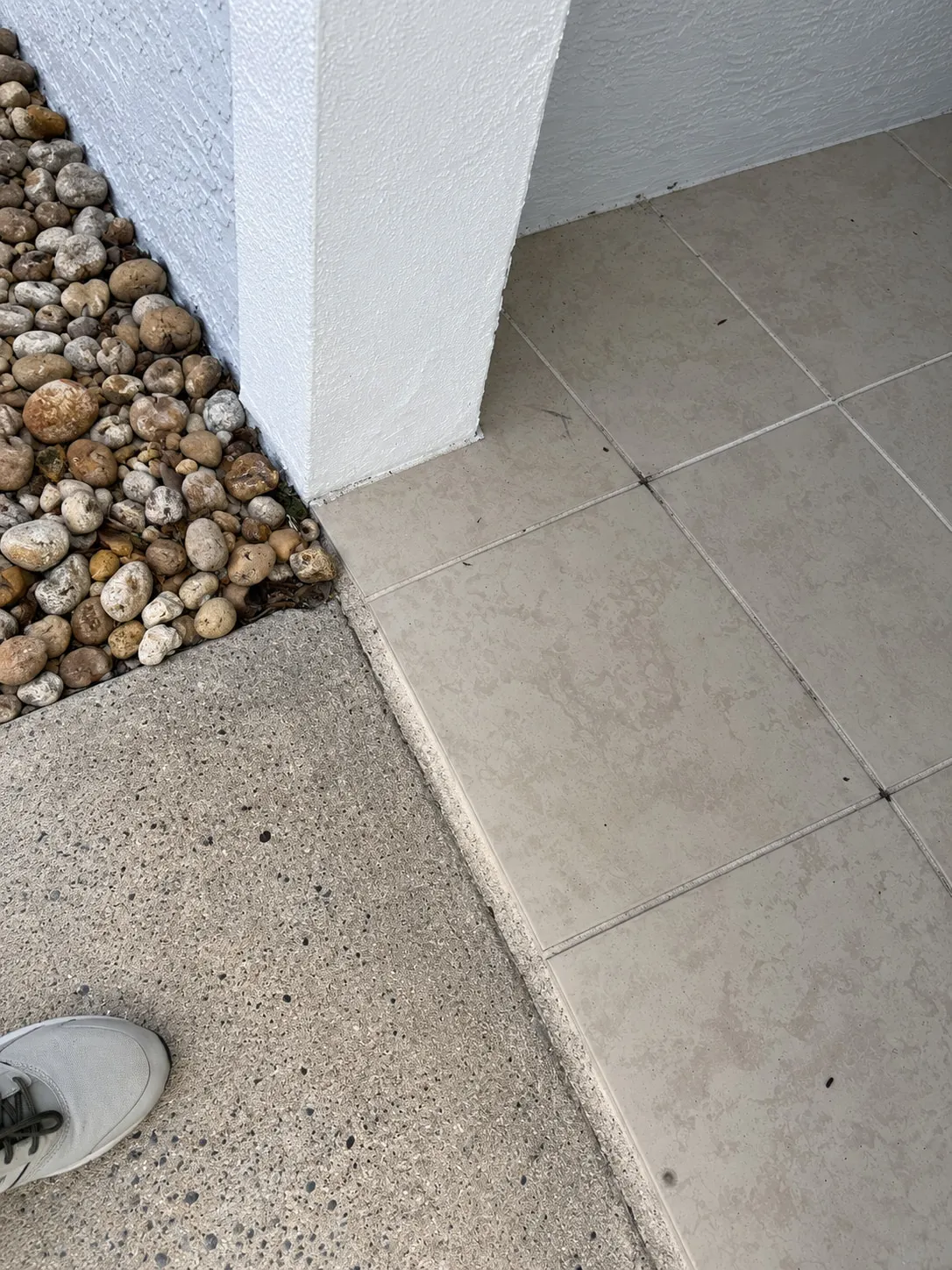 Corner of an outdoor tile entryway showing grey staining next to a river rock bed, before cleaning