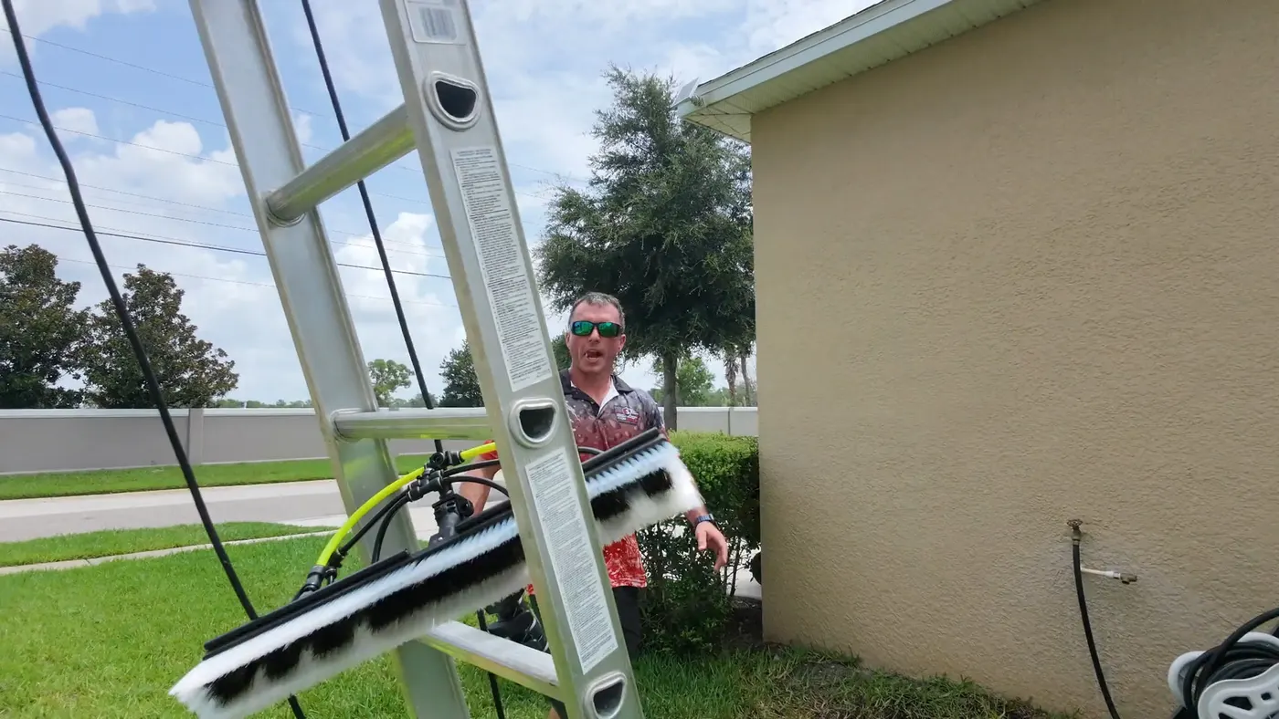 Extension ladder and long-reach cleaning brush set against the side of a home before rust stain treatment begins