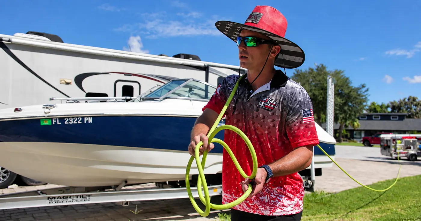 Iron Shield technician coiling the cleaning hose at the side of a property, a boat on its trailer parked behind