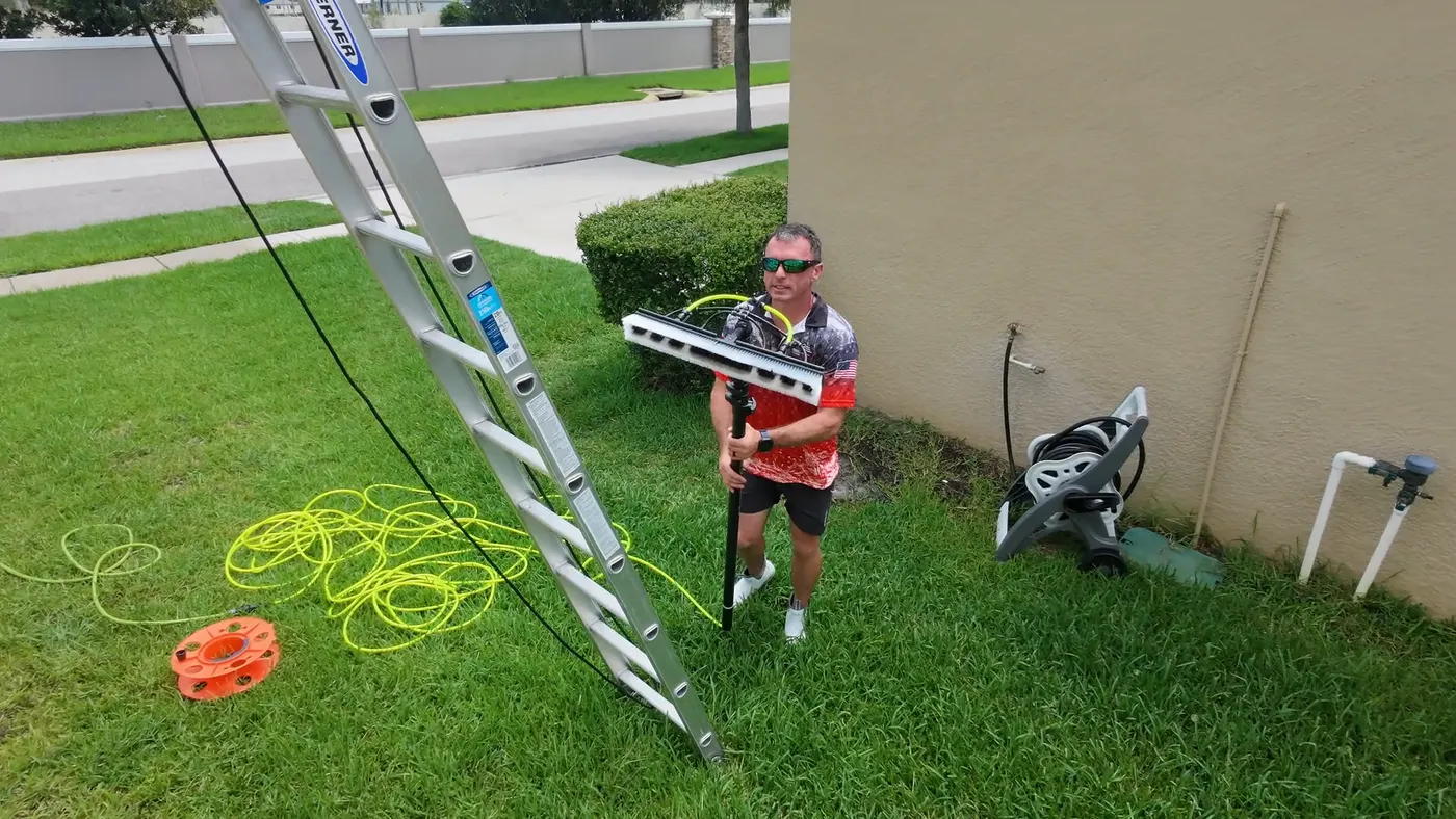 Iron Shield technician carrying the application brush across the lawn, hose coiled ready beside the stucco wall
