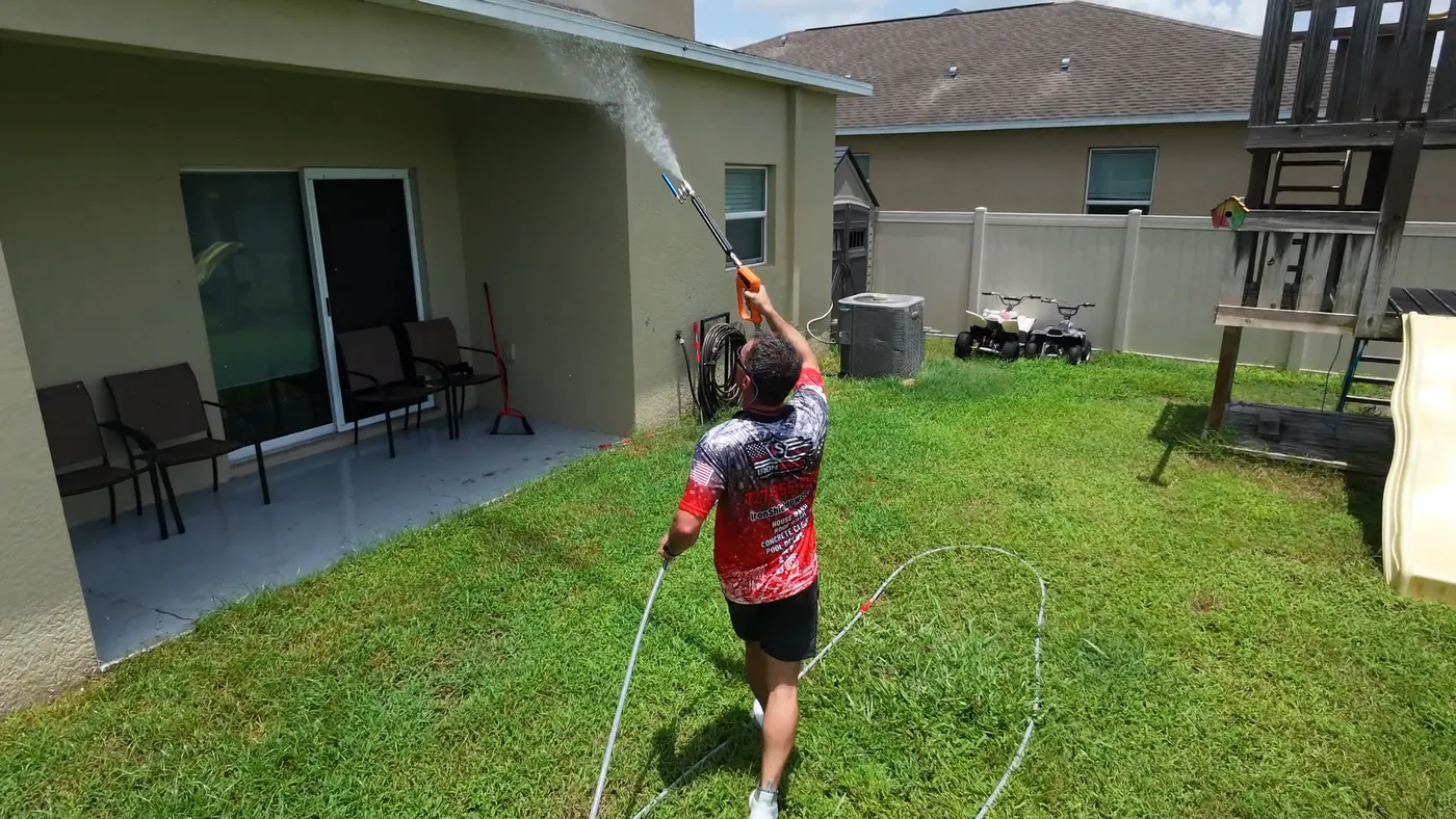 Iron Shield technician cleaning the rear wall of a home next to the backyard play structure
