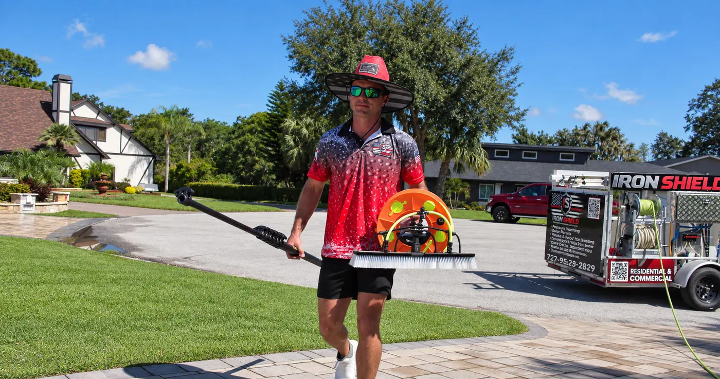 Iron Shield technician walking a cleaning line across the front lawn, the company trailer parked at the kerb