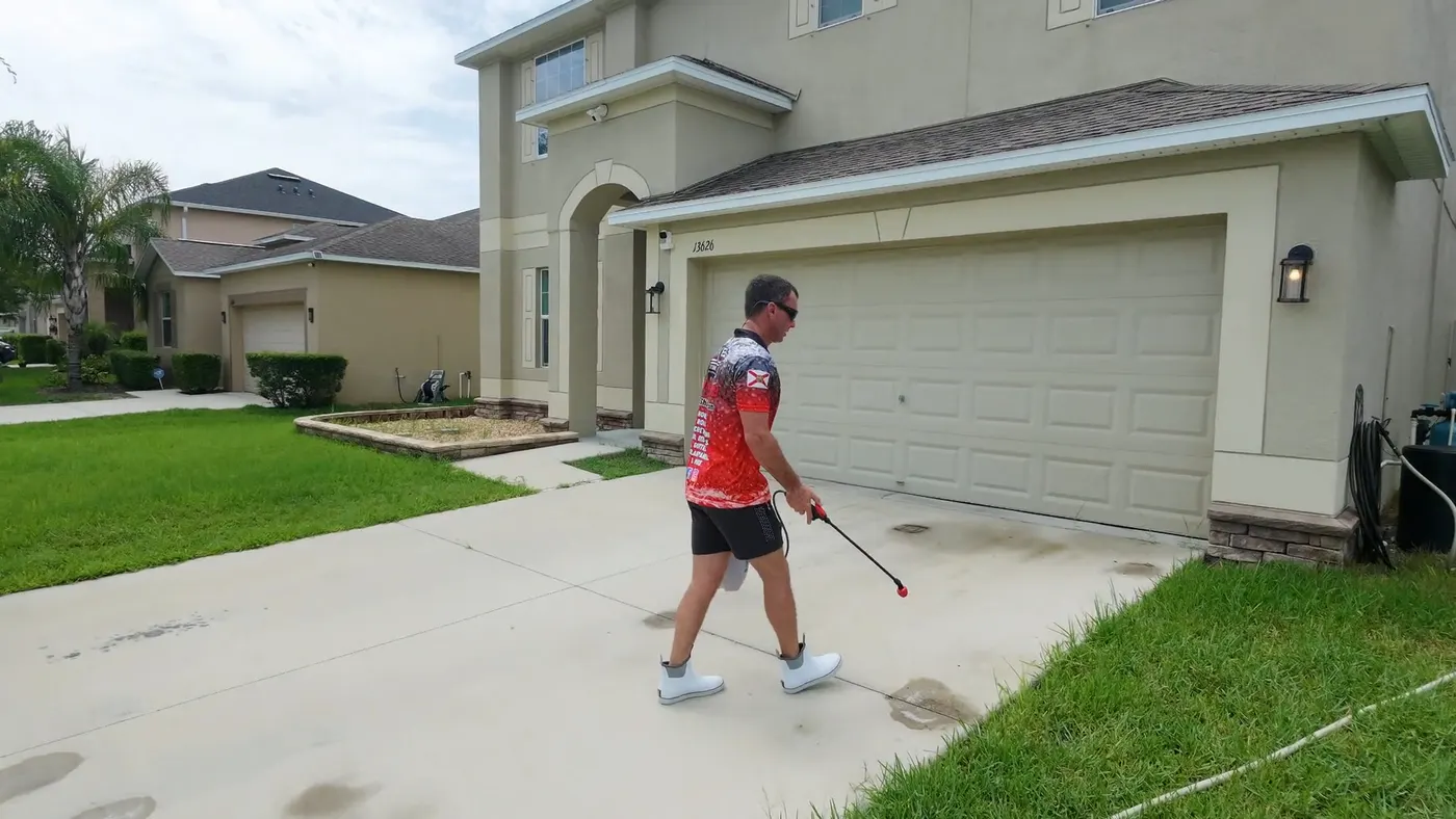 Iron Shield technician spot-treating stained areas of a concrete driveway beside a Hudson home
