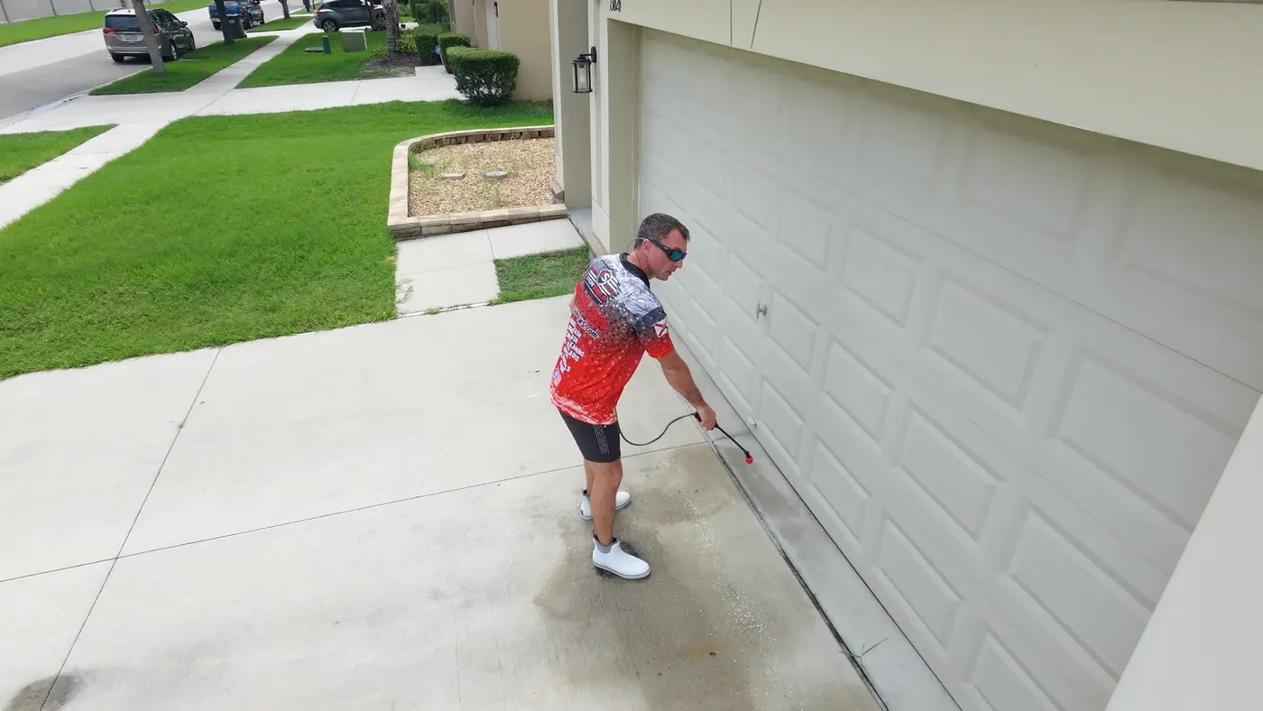 Iron Shield technician moving across a driveway with a handheld sprayer, loosening embedded grime ahead of the wash